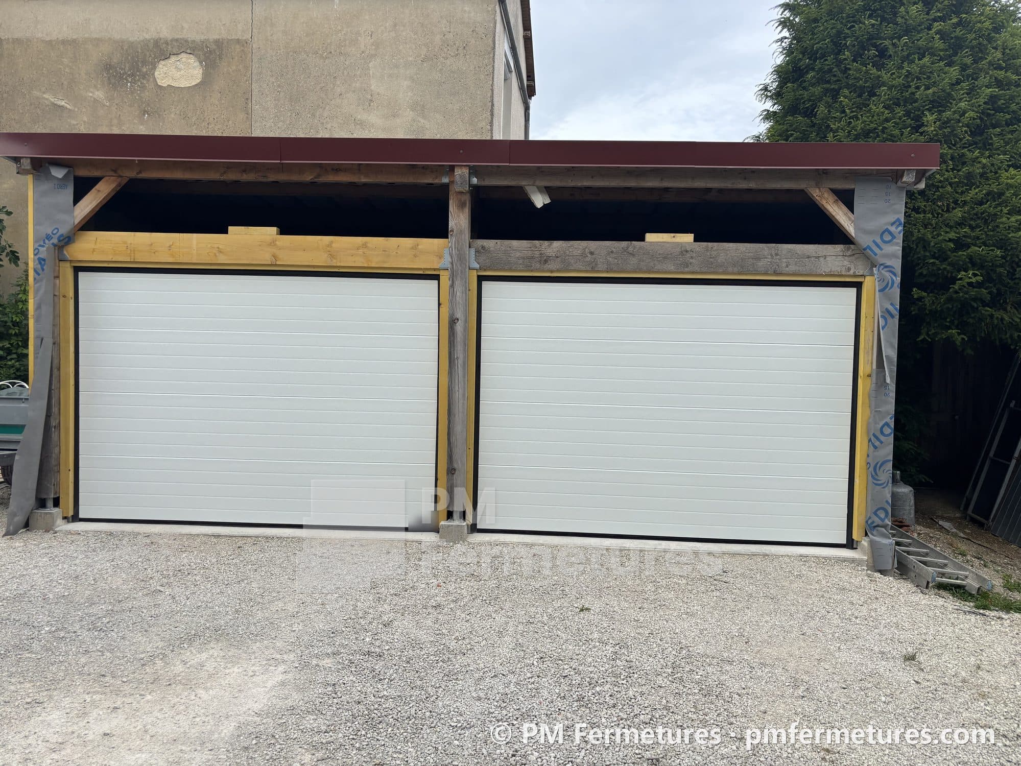 Deux portes de garage sectionnelles blanches côte à côte sous un abri en bois