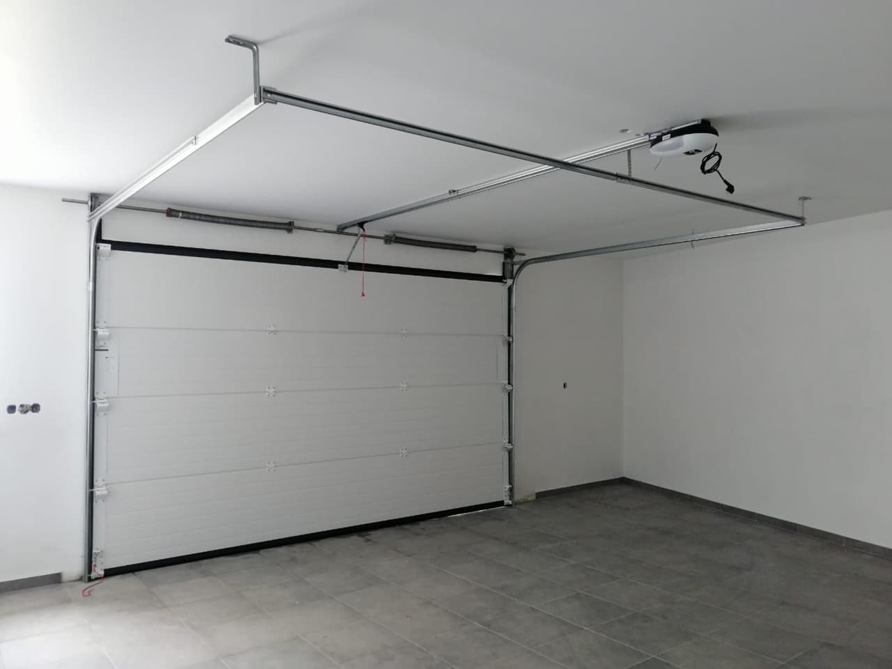 Porte de garage sectionnelle blanche motorisée, vue intérieure avec rails et moteur