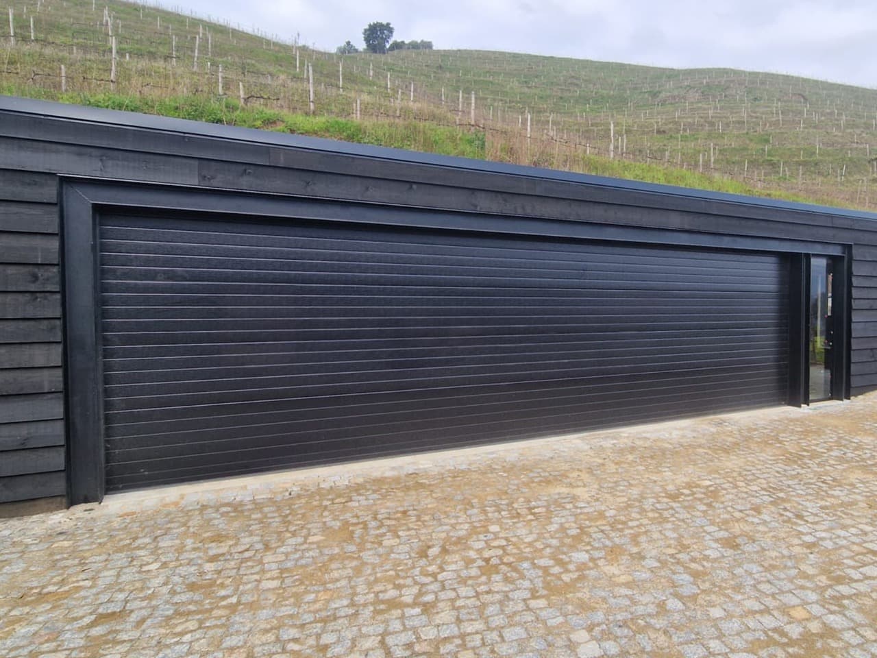 Porte de garage sectionnelle noire grande largeur sur double garage, avec porte de service