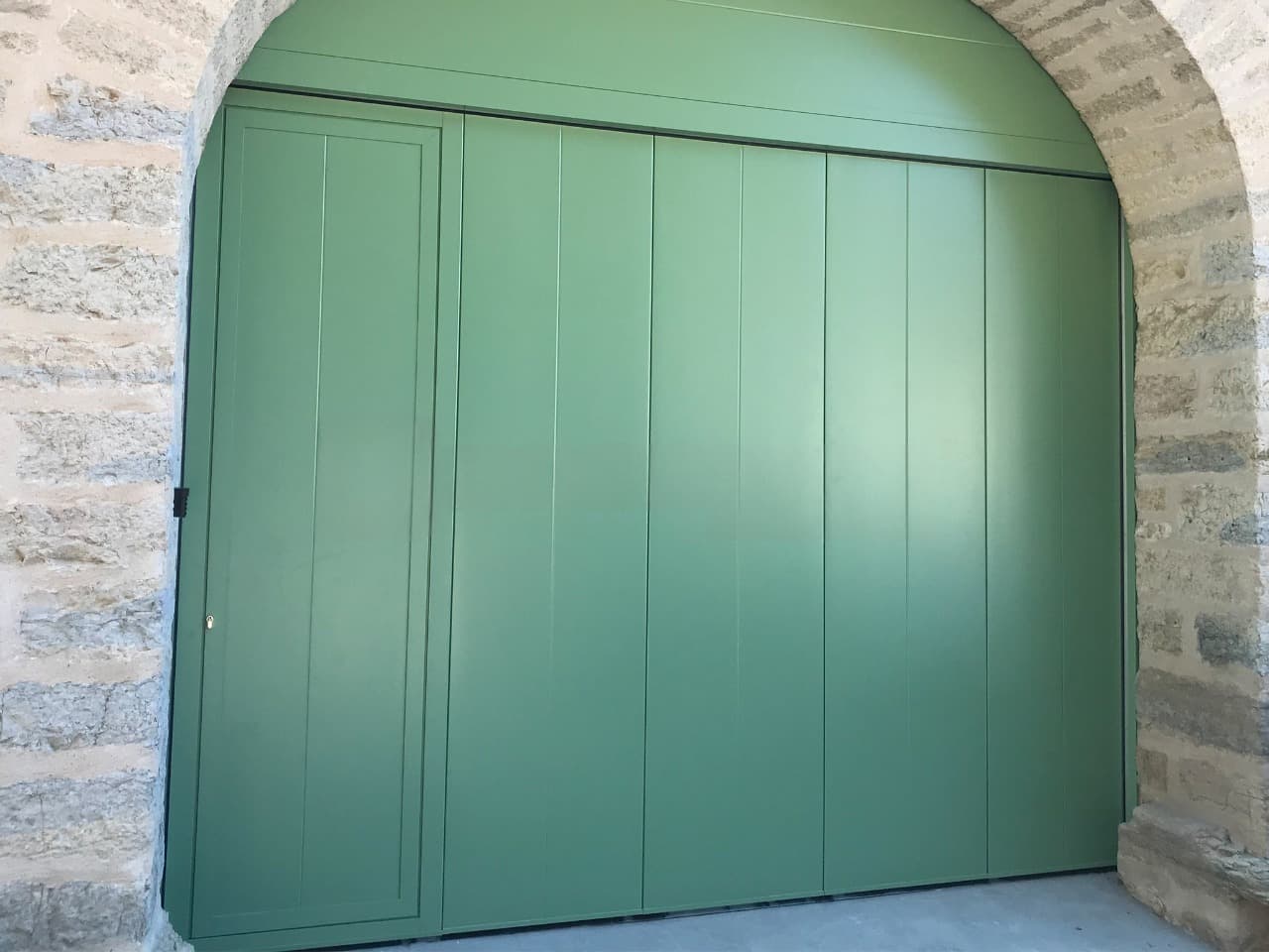 Porte de garage latérale battante verte avec portillon intégré sous arche en pierre