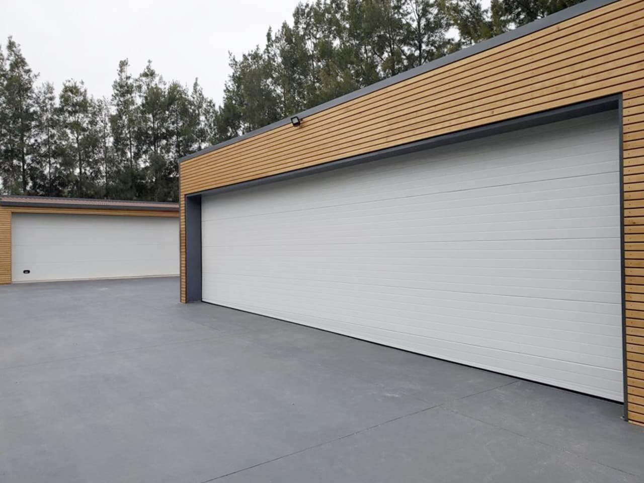 Garage résidentiel moderne avec porte de garage sectionnelle blanche et bardage bois
